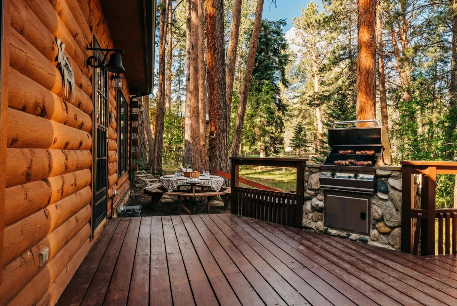 The deck at My Story with a built-in stone grill and a picnic table set among ponderosa pines.