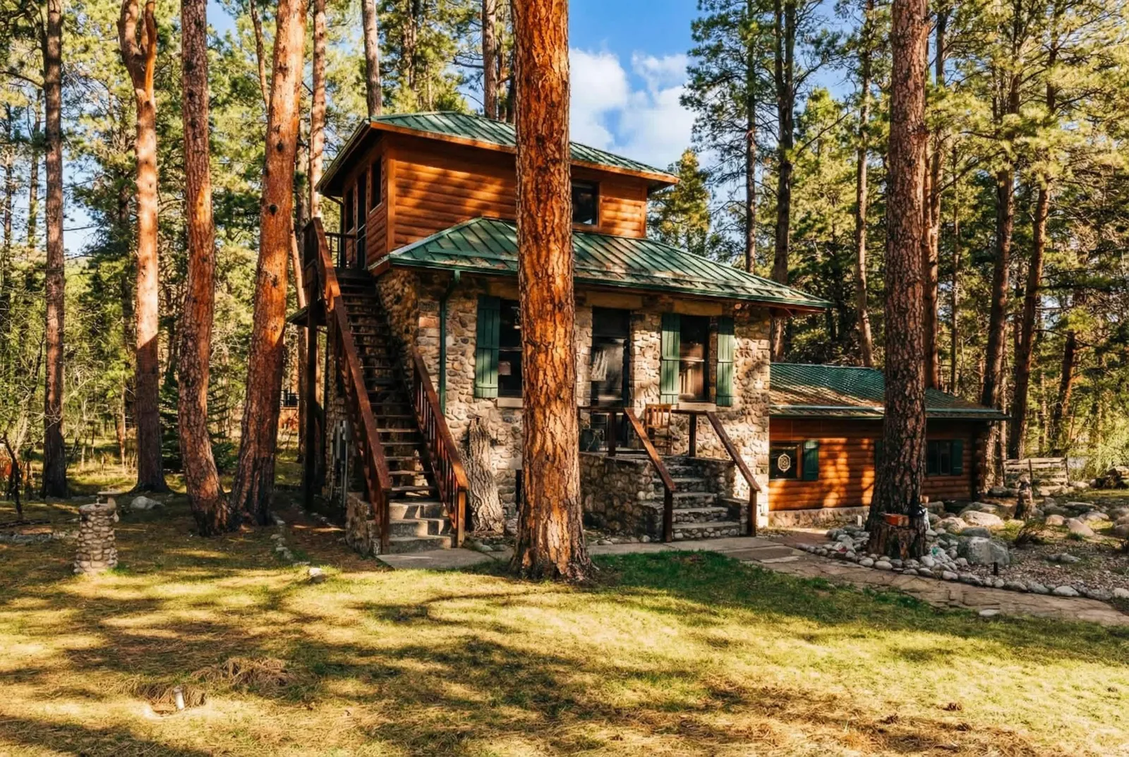 My Story, a historic stone-and-log cabin with a green metal roof among ponderosa pines in Story, Wyoming.