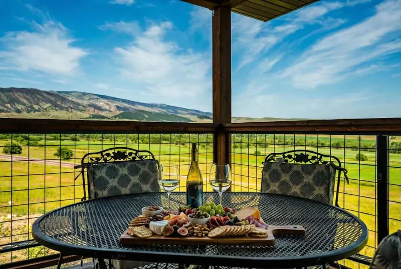 Covered deck with a table set for two and a view of green pasture and the Bighorn foothills
