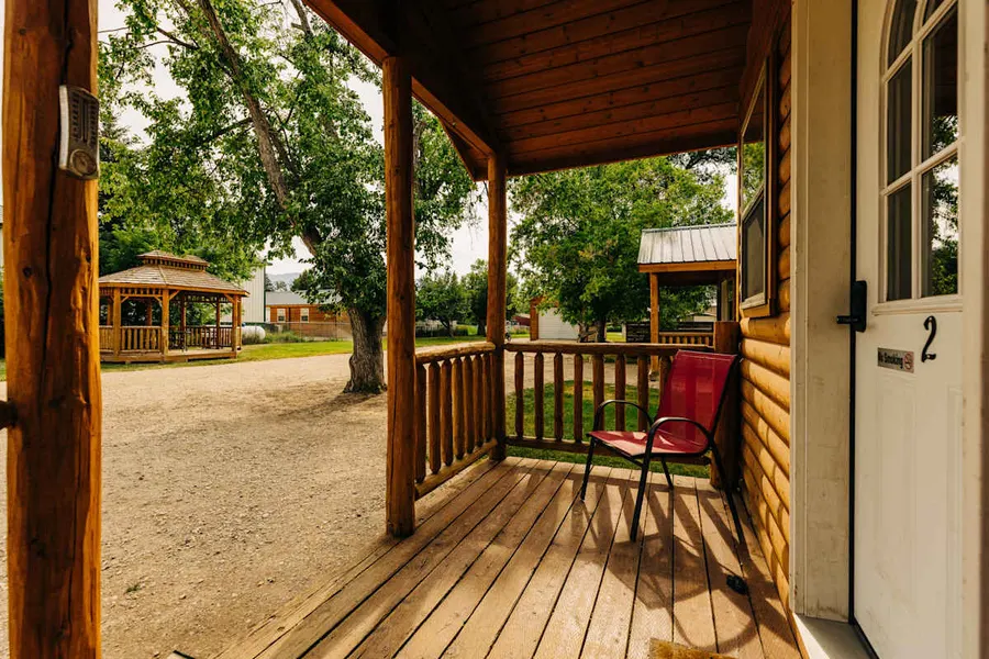 Front porch of a log cabin with a red chair, gravel drive and a gazebo across the lot in Dayton